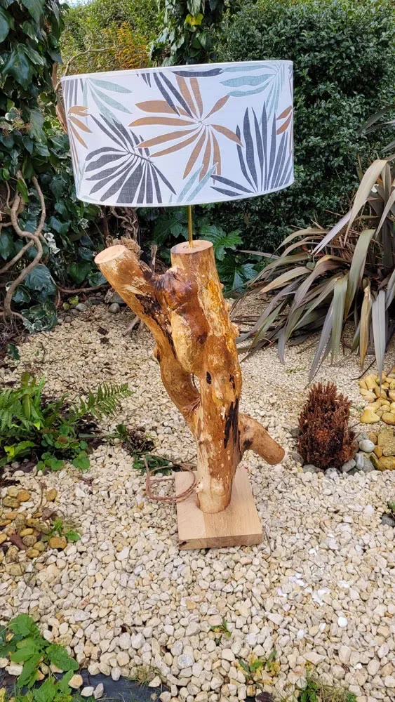 Lampe en bois flotté à deux branches avec abat-jour à motif de feuilles, photographiée au jardin